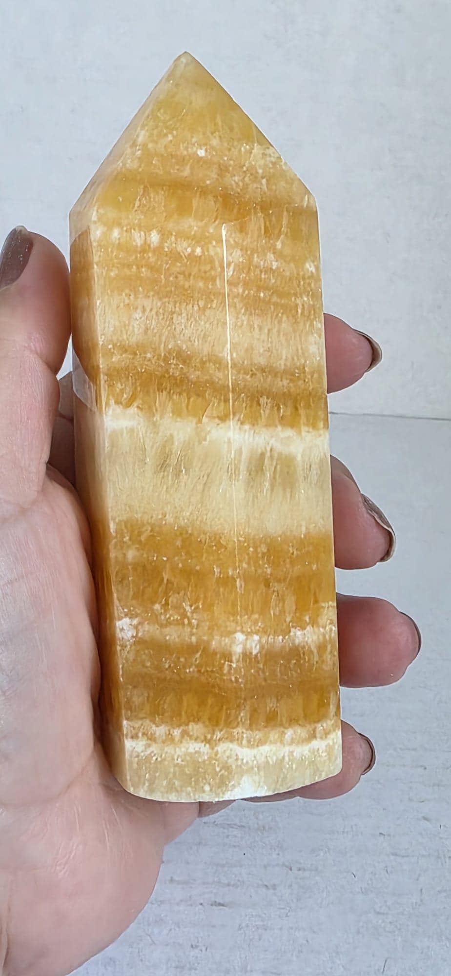Honey-yellow calcite tower mineral point held in hand, faceted polished tip with banding.
