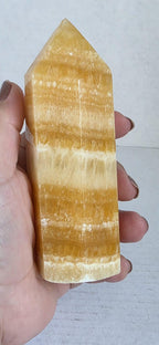 Honey-yellow calcite tower mineral point held in hand, faceted polished tip with banding.