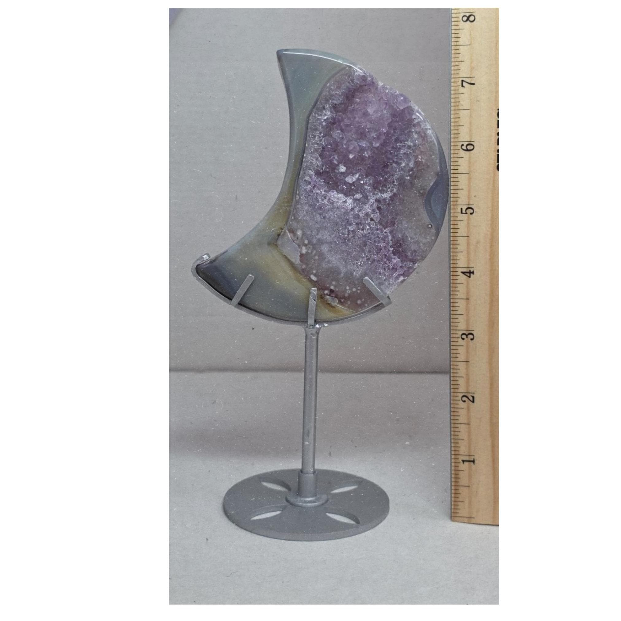 Crescent moon purple druzy agate geode on stand beside measuring tape