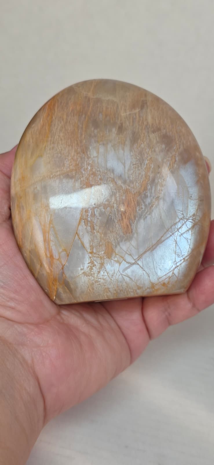 Polished peach moonstone crystal, rounded dome held in hand with light striations