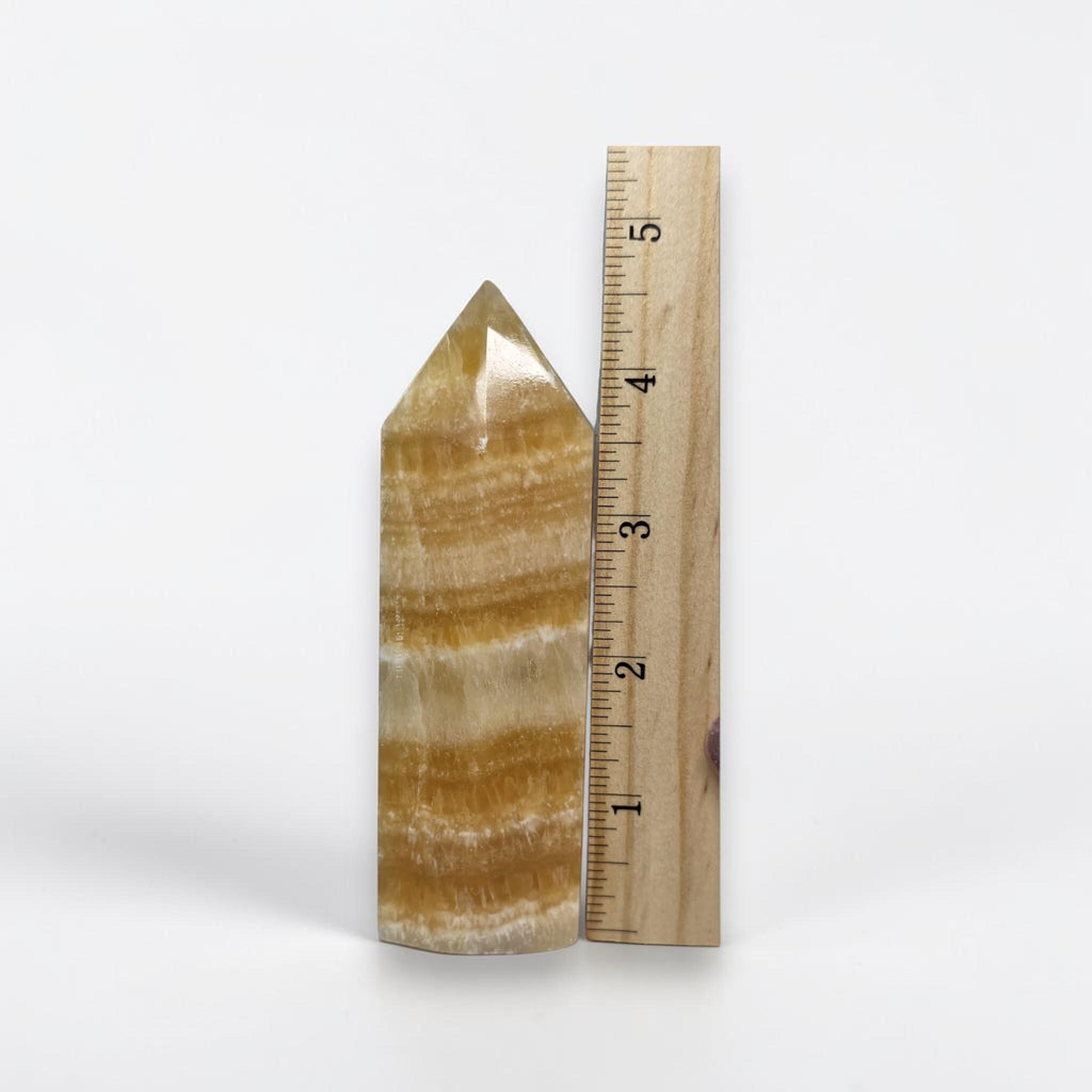 Honey-yellow calcite tower mineral point with banded layers, shown beside measuring ruler.