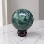 Dark green fluorite crystal sphere on glossy dark pedestal stand, smooth reflective