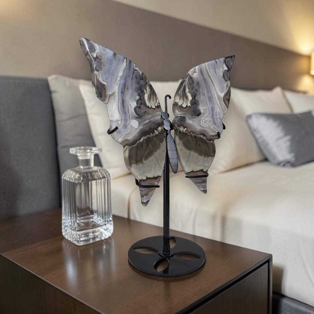 Butterfly sculpture on a stand next to a clear glass vase on a wooden table with a blurred sofa in the background.