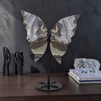 Butterfly-shaped decorative piece on a stand with books and crystal object in the background.
