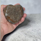 Heart-shaped stone held in a hand on a speckled surface