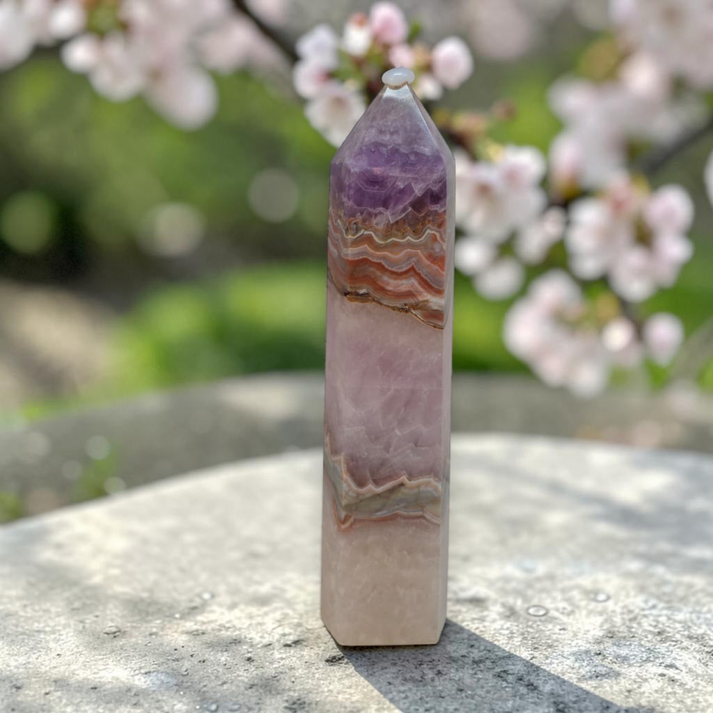Amethyst gemstone tower with tan lace banding and faceted tip outdoors