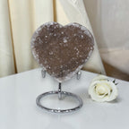 Heart-shaped crystal on a stand with a white rose on a white surface