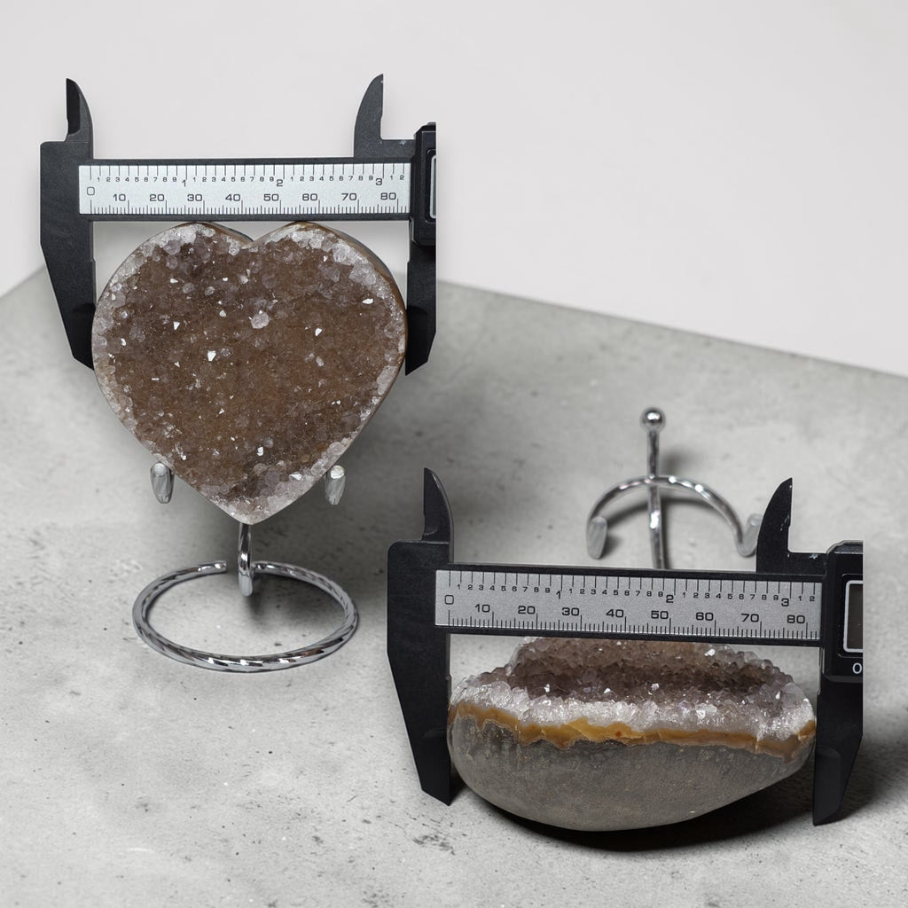 Two heart-shaped geode crystals with rulers for scale on a gray surface