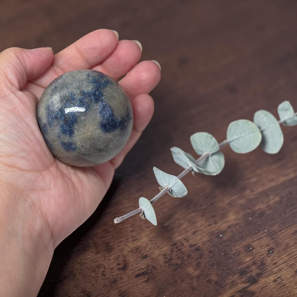 Blue speckled granite crystal sphere in hand beside small decorative stones