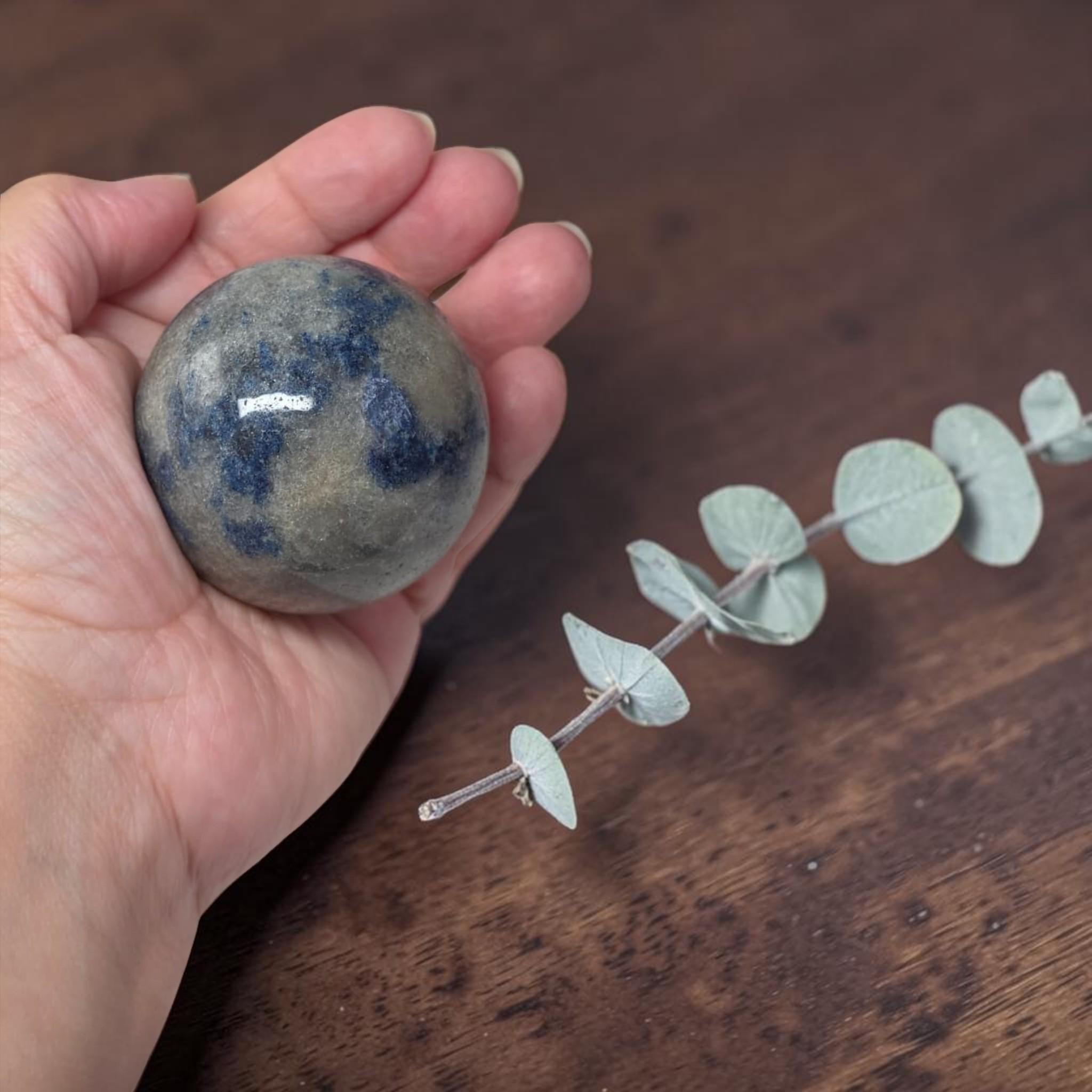 Blue speckled granite crystal sphere in hand beside small decorative stones