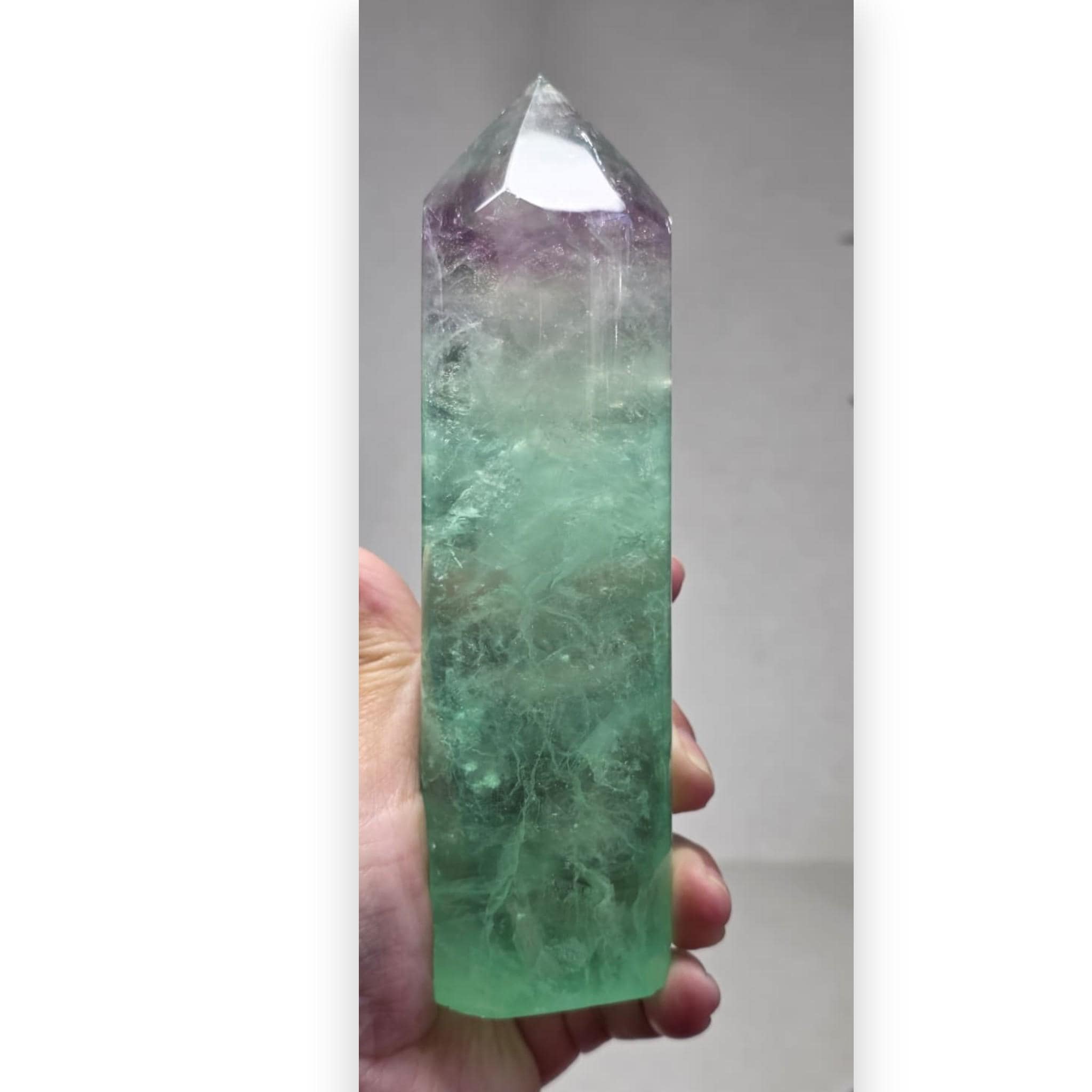 Green fluorite crystal tower held in hand, purple top, polished pointed prism
