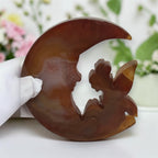 Banded agate moon fairy sculpture on black metal stand, front view with garden background
