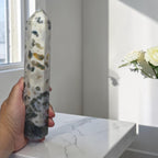 Crystal obelisk tower held in hand, white body with dark green and gold mottling