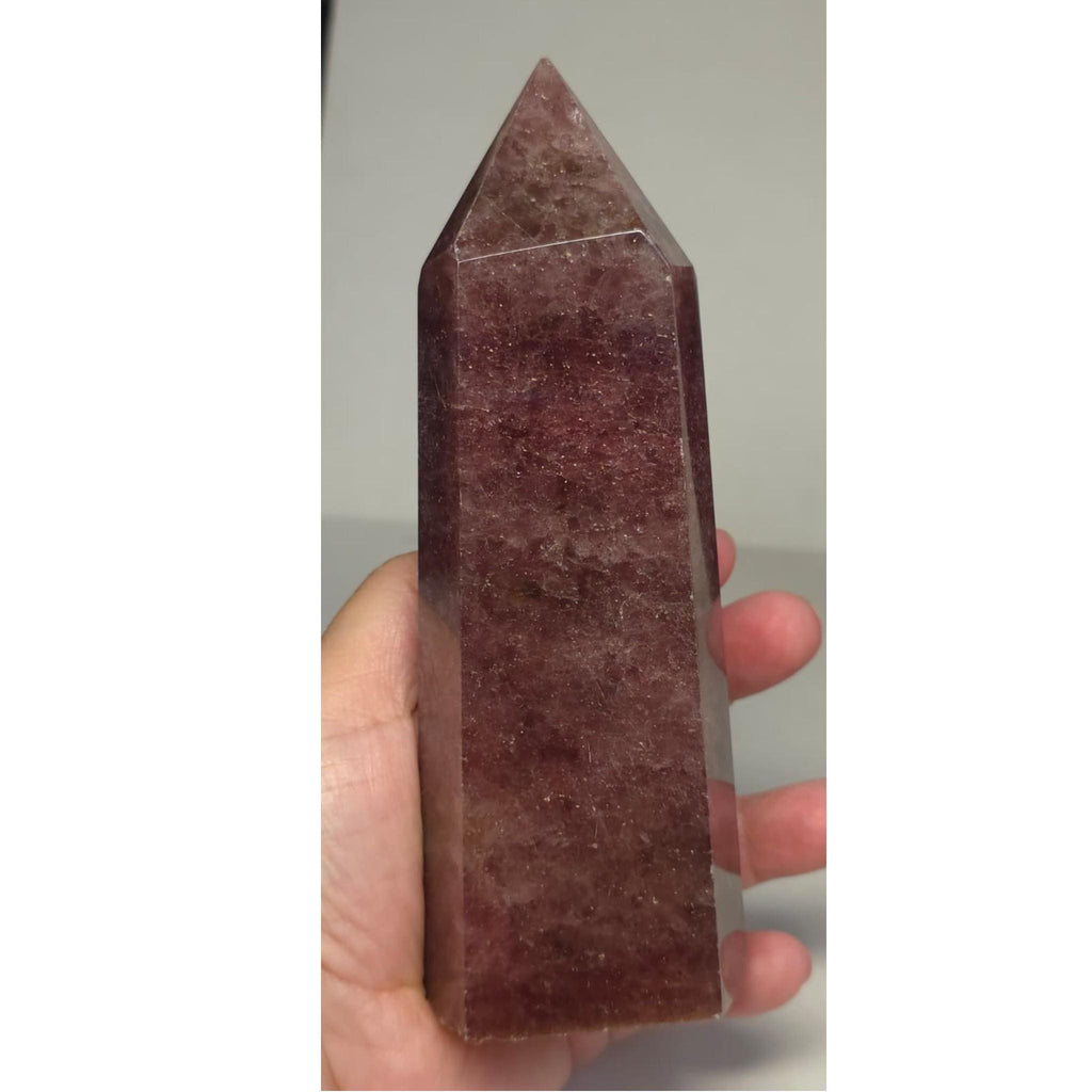 Deep red quartz crystal point tower held in hand, pointed tip up