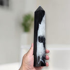 Hand holding a large black agate quartz tower to show scale, with sparkling druzy quartz cavity visible across the full length of the stone