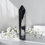 Black agate quartz tower displayed as home decor on a white side table next to white roses in a glass vase, modern living room setting