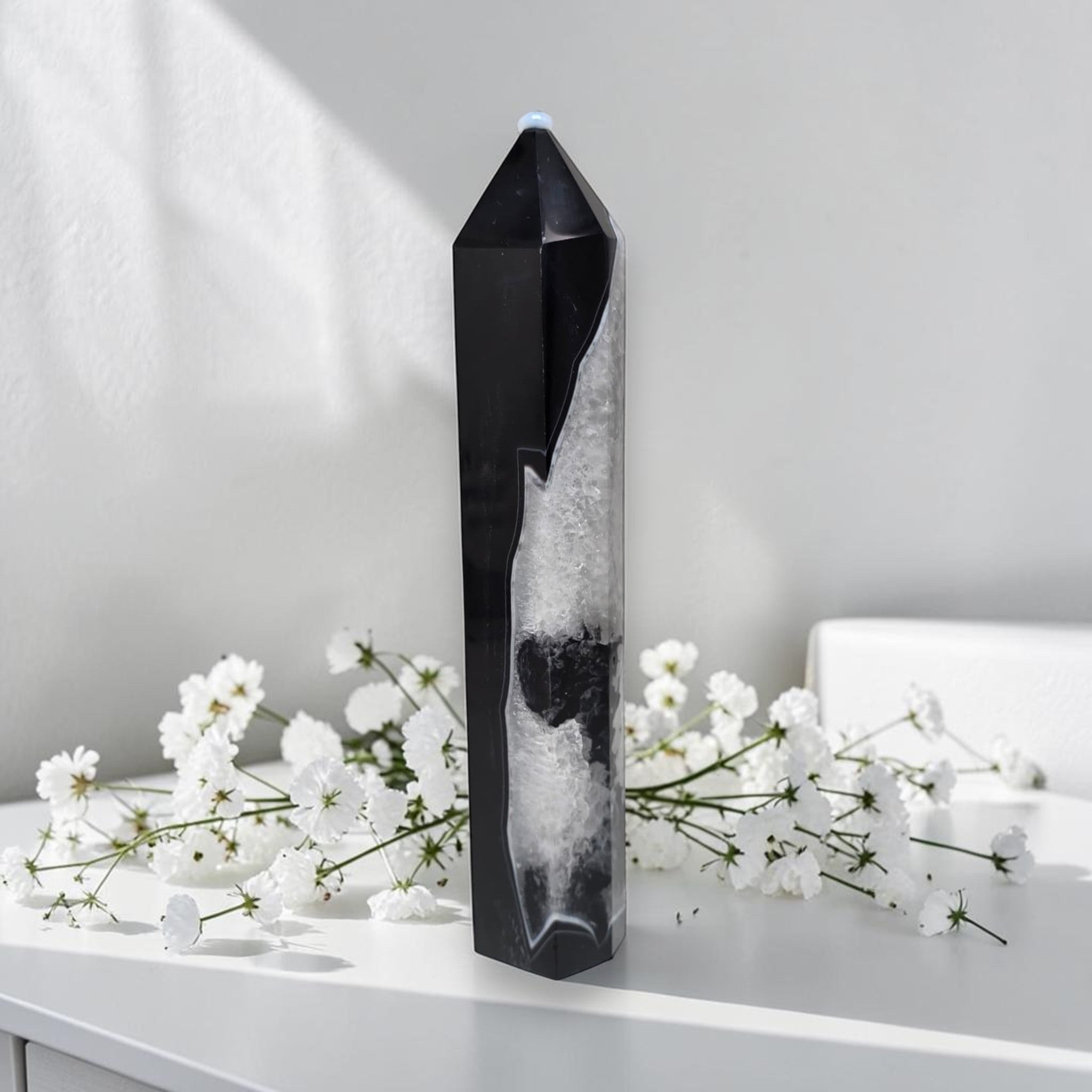 Black agate quartz tower displayed as home decor on a white side table next to white roses in a glass vase, modern living room setting
