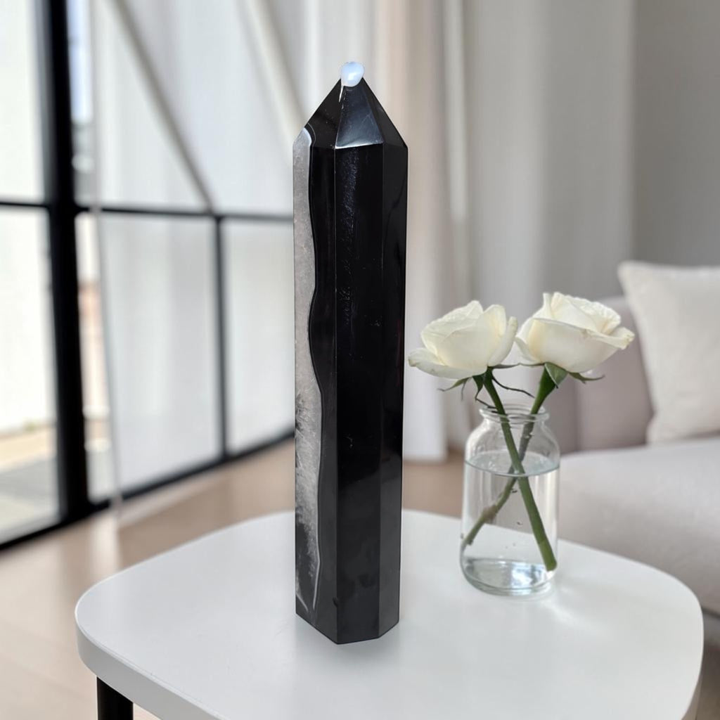 Side profile of black agate quartz tower on a white table, showing the sleek polished obelisk form with natural quartz druzy detail