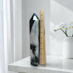 Black agate quartz tower next to a ruler showing approximately 8 inches in height, on a white marble surface with orchid flowers