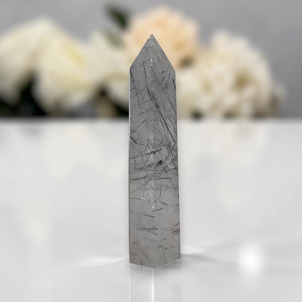 Gray rutilated quartz crystal tower with scattered dark needle-like inclusions