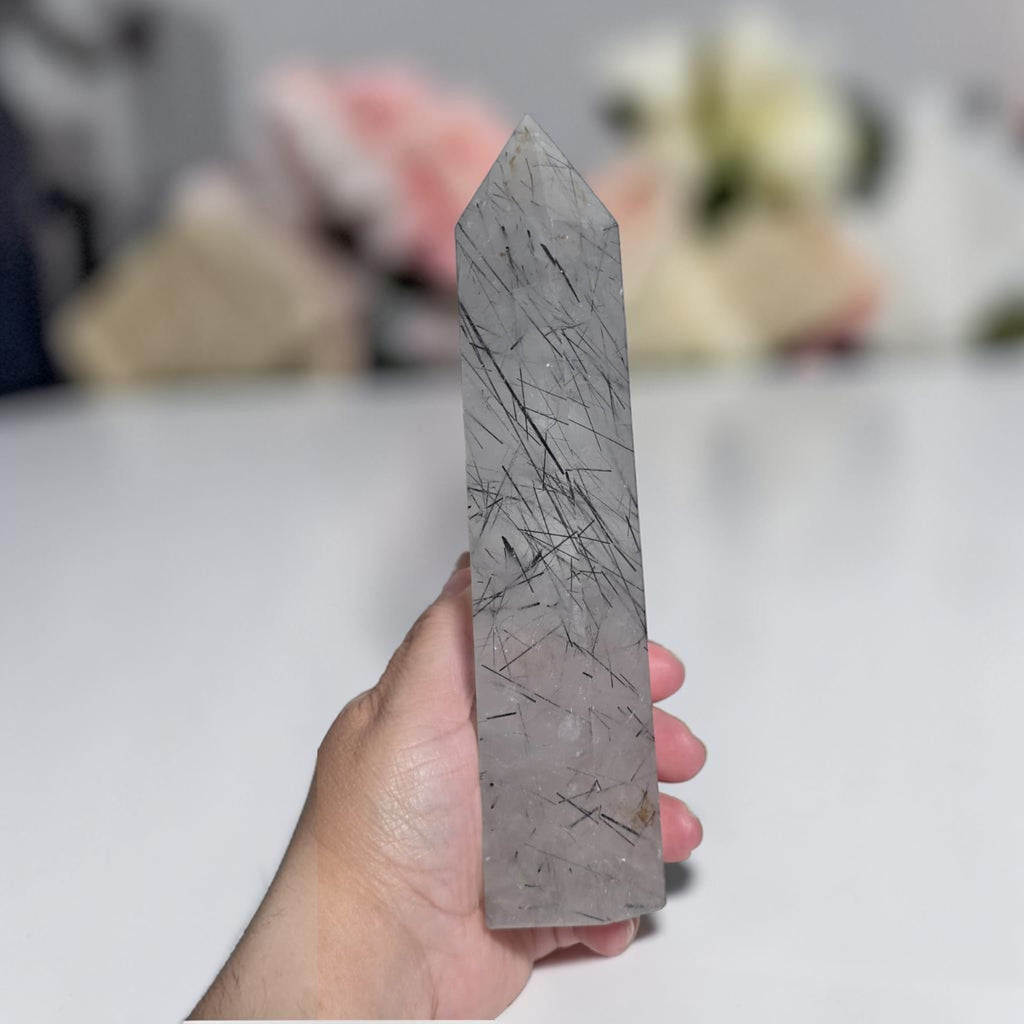 Handheld gray rutilated quartz tower with dark needle inclusions and pointed tip