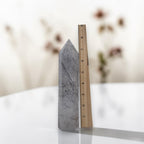 Rutilated quartz obelisk tower, gray with dark needle rutiles; measured against ruler