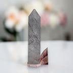 Gray rutilated quartz crystal tower with dark needle-like inclusions and pointed top