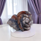 Rose agate carving with sculpted petals in dark gray-blue, purple tones, and orange highlights
