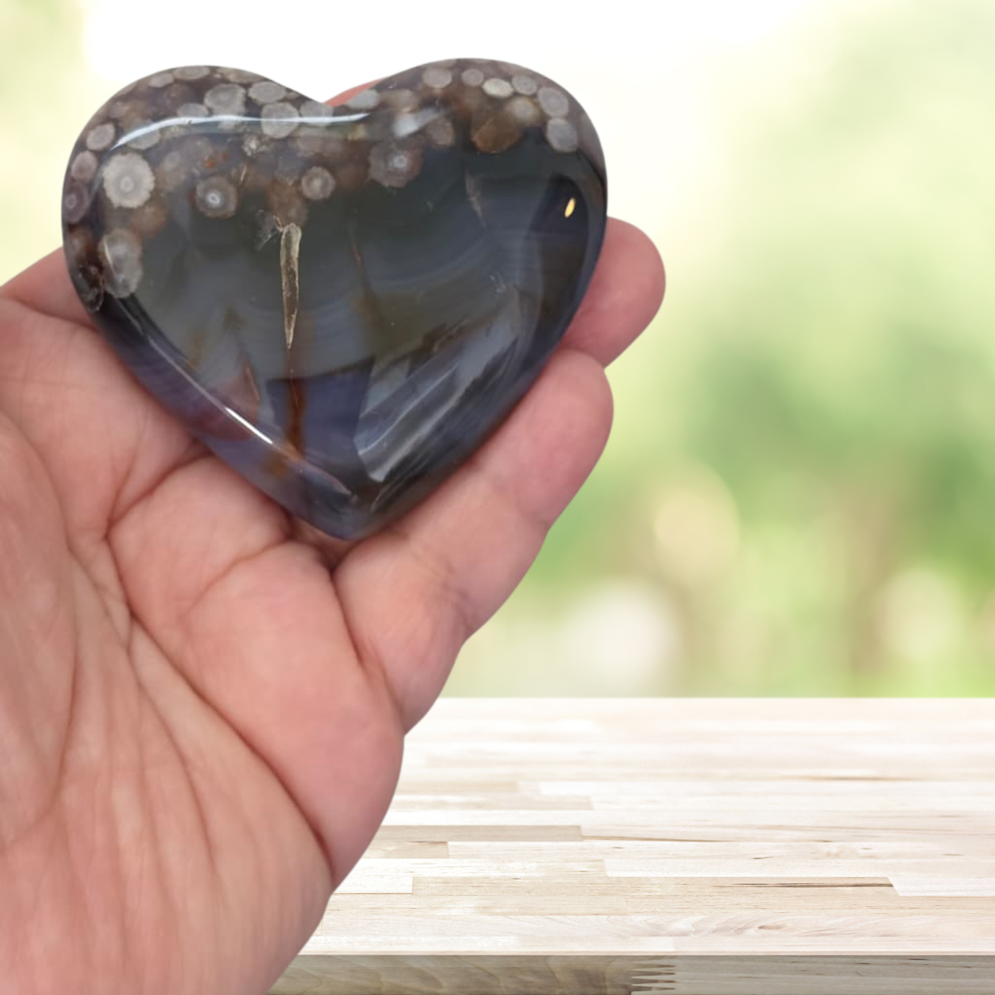 Heart-shaped agate stone held in a hand with a blurred natural background