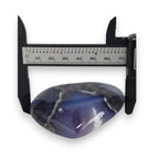 Blue agate stone with a caliper measuring its size on a white background
