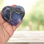 Heart-shaped purple stone held in a hand with a blurred natural background