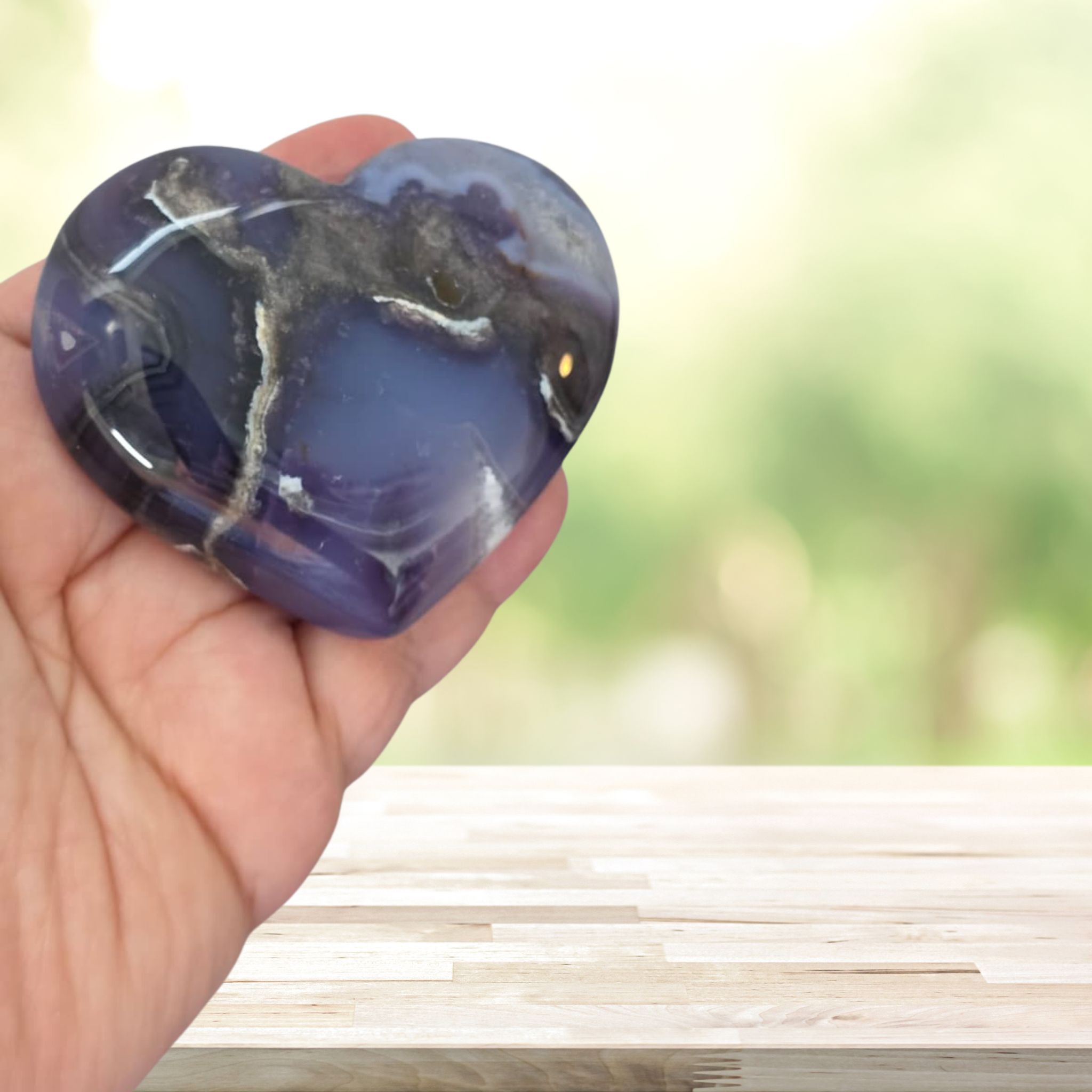 Heart-shaped purple stone held in a hand with a blurred natural background