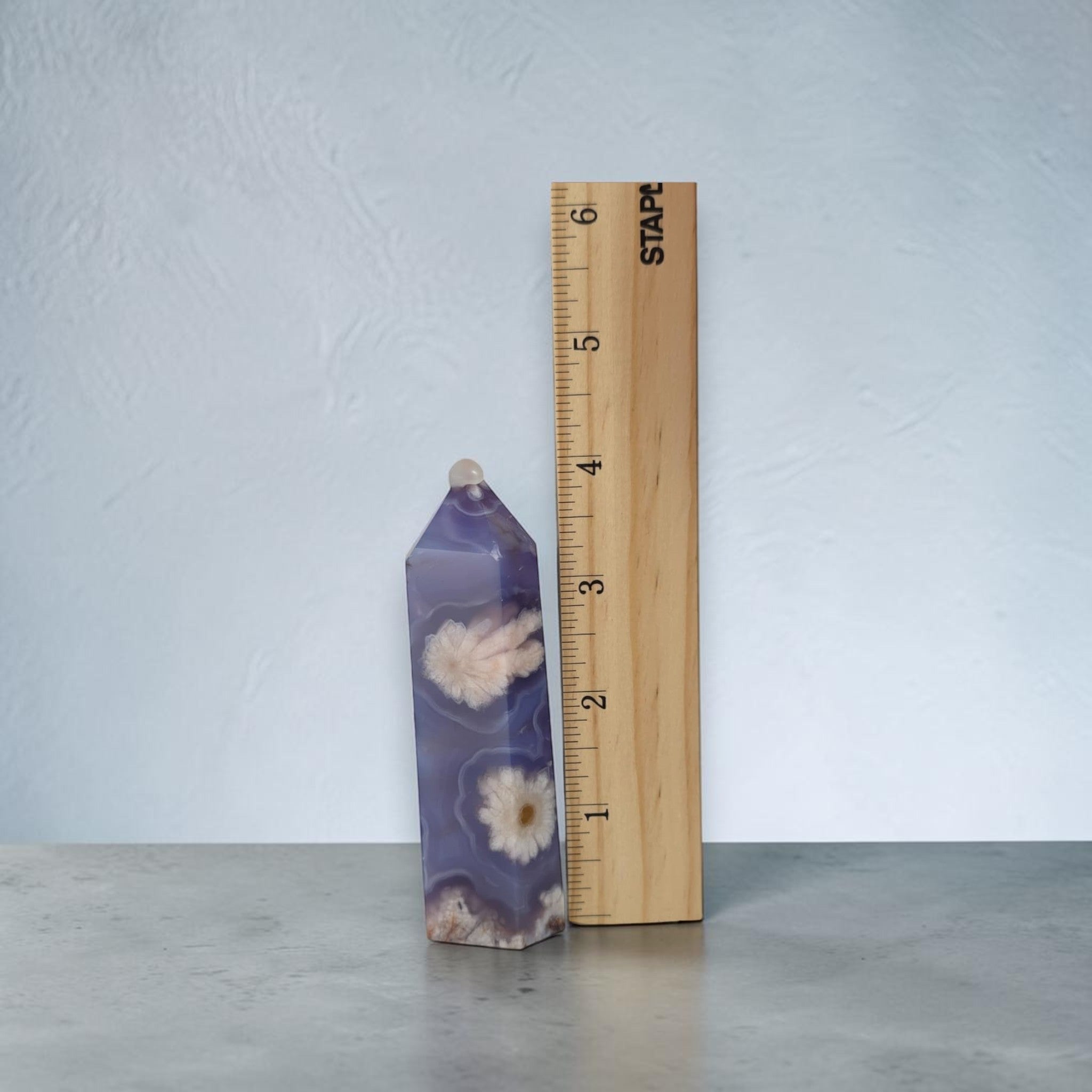 Decorative purple object with floral patterns next to a wooden ruler on a light gray background