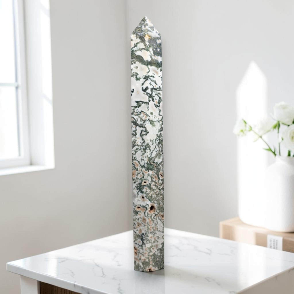 Moss agate obelisk point on display, green moss patterns in white stone.