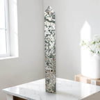 Moss agate obelisk point on display, green moss patterns in white stone.