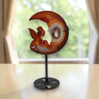View from the side: amber moon crystal sculpture with fairy carving and druzy geode, on stand