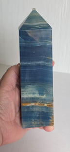 Blue stone crystal obelisk held in hand, pointed top with banded wave patterns