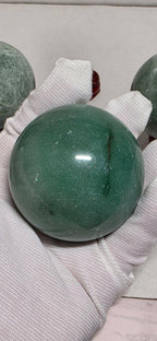 Green crystal sphere cradled in white gloves, maroon round base, glossy orb