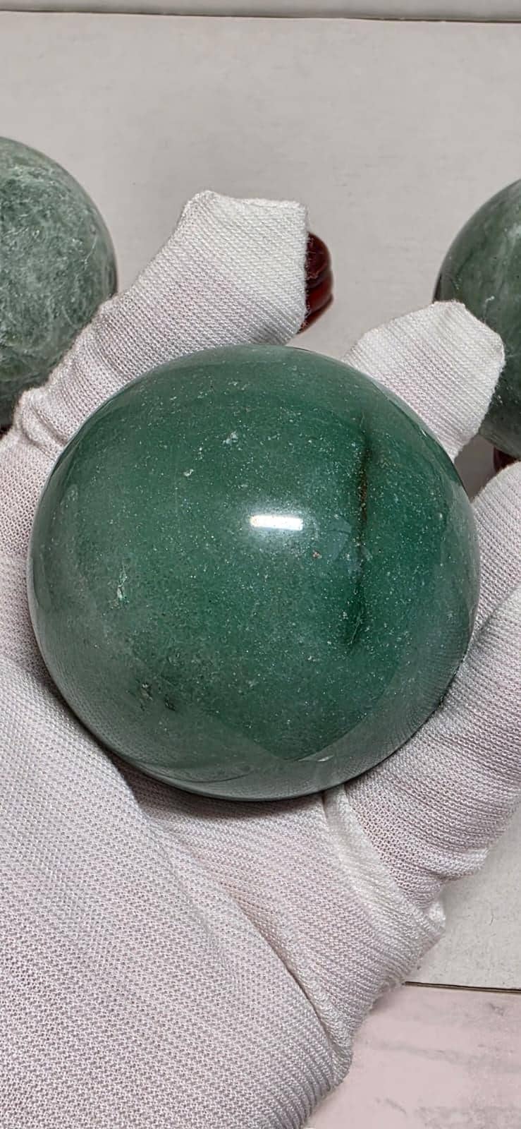 Green crystal sphere cradled in white gloves, maroon round base, glossy orb