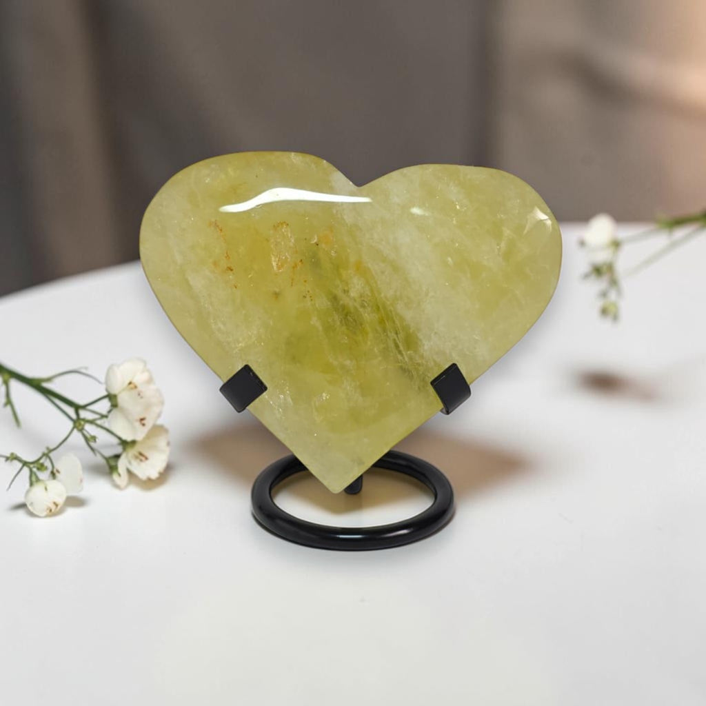 Heart-shaped green stone on a stand with white flowers on a light surface