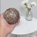 Coral jasper sphere 80mm in hand, mottled brown with veined gemstone pattern