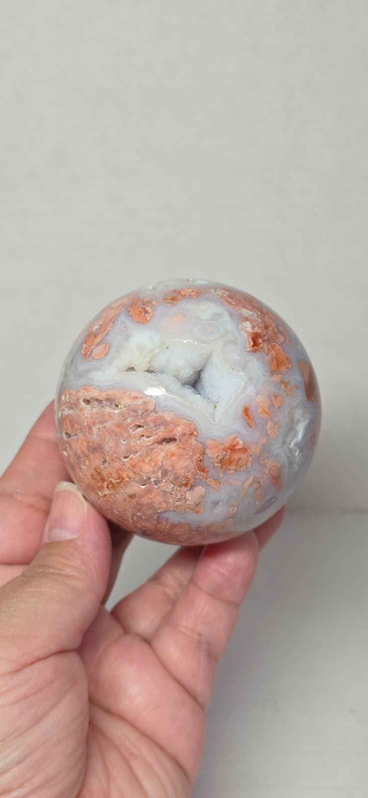 Agate sphere held in hand, blue-gray with orange-brown stone patterns