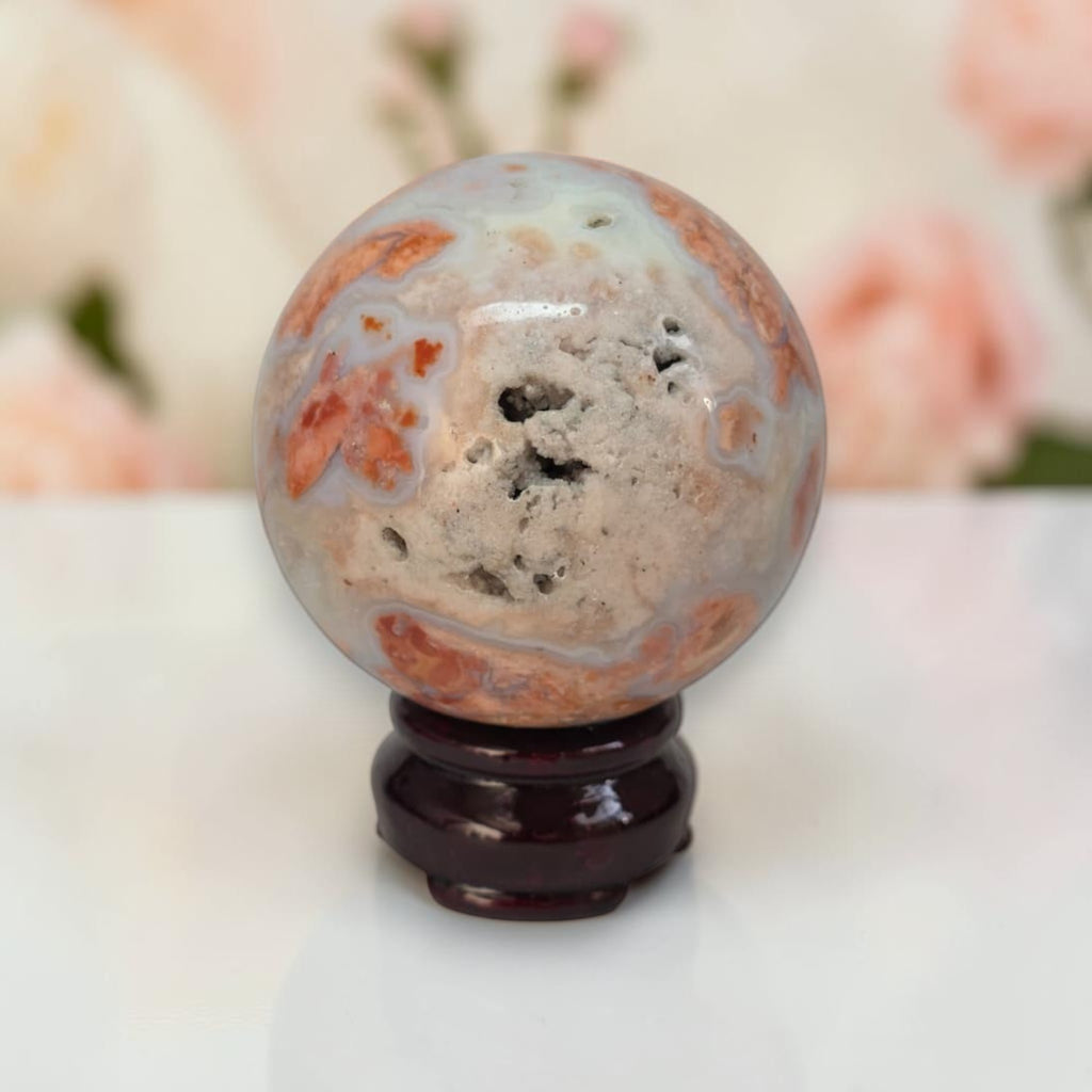 Multicolor agate sphere with orange, gray, and white patches on dark wooden base