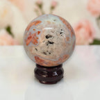 Multicolor agate sphere with orange, gray, and white patches on dark wooden base
