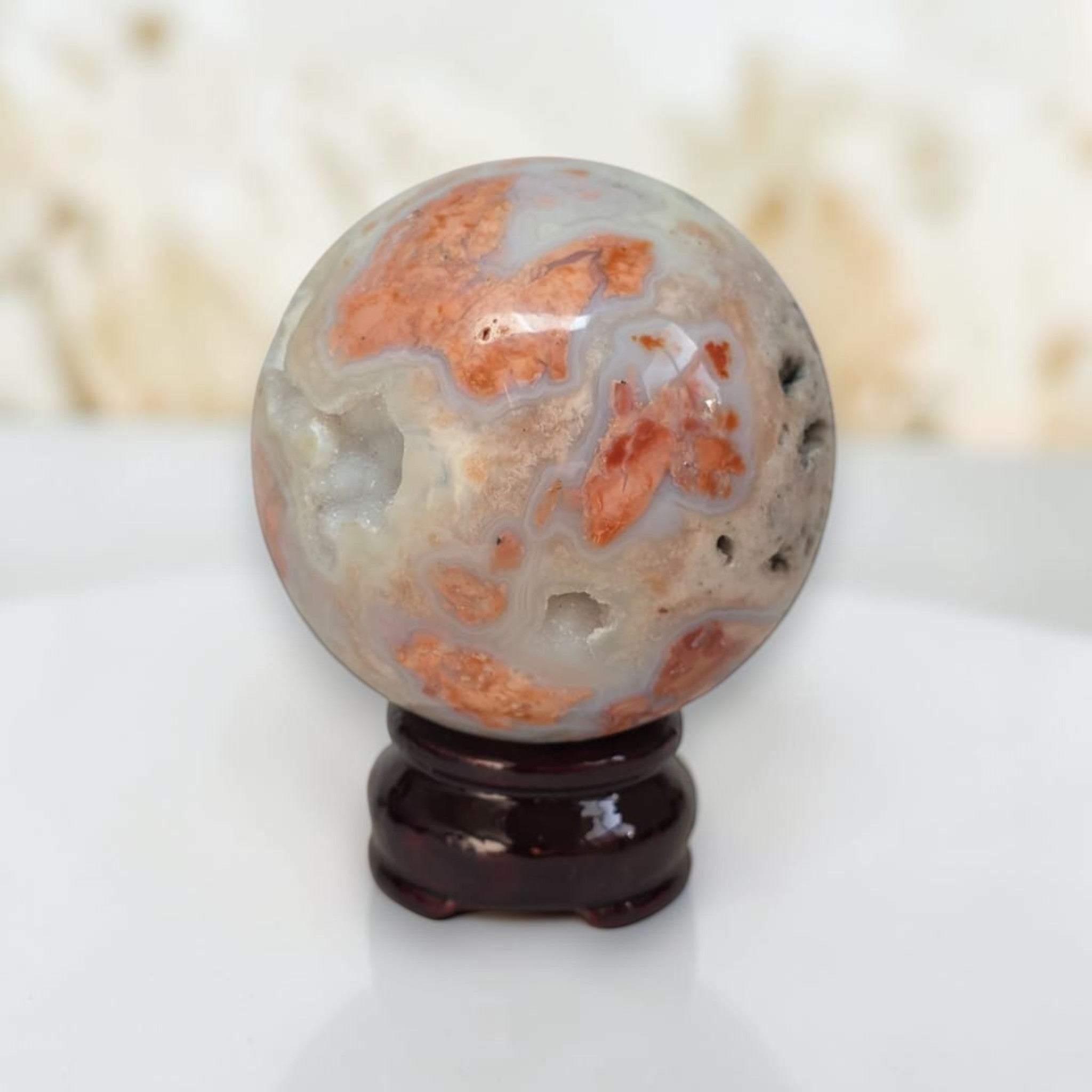 Agate sphere with cloudy white, gray, and orange streaks on dark wood base