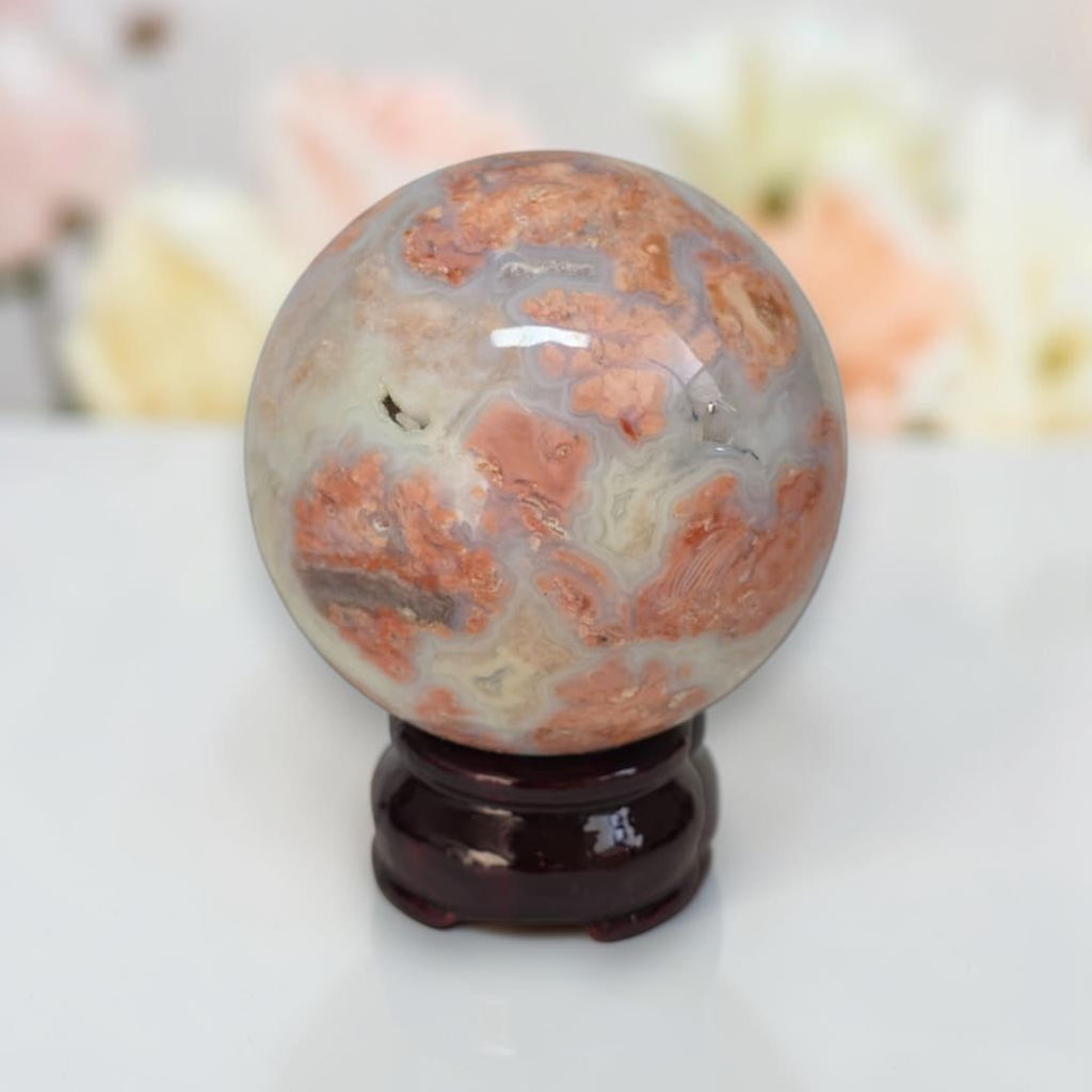 Cotton candy agate sphere with orange patterns and white base on dark stand