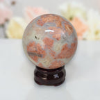 Cotton candy agate sphere with orange patterns and white base on dark stand