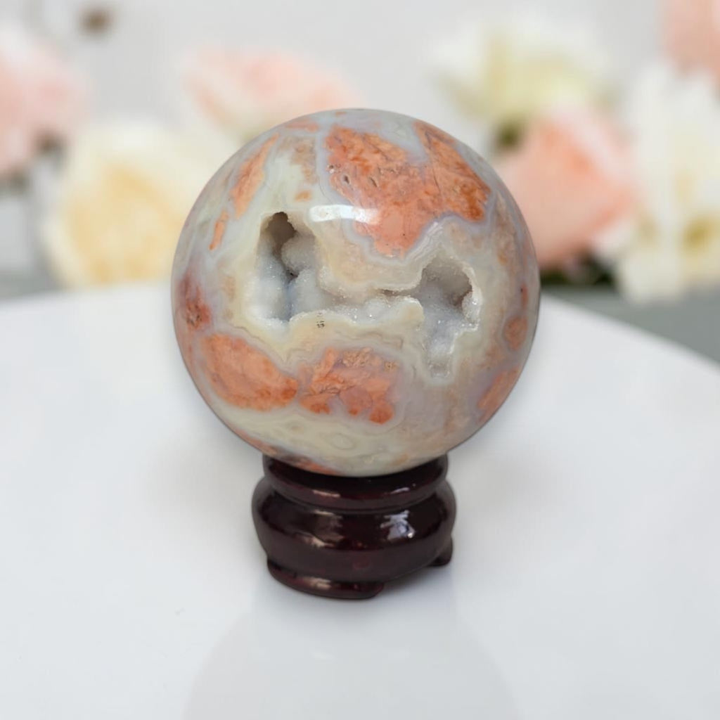Agate sphere with white and orange swirls, glossy finish on dark wood stand