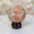 Speckled agate sphere with warm orange bands and creamy white areas on dark stand