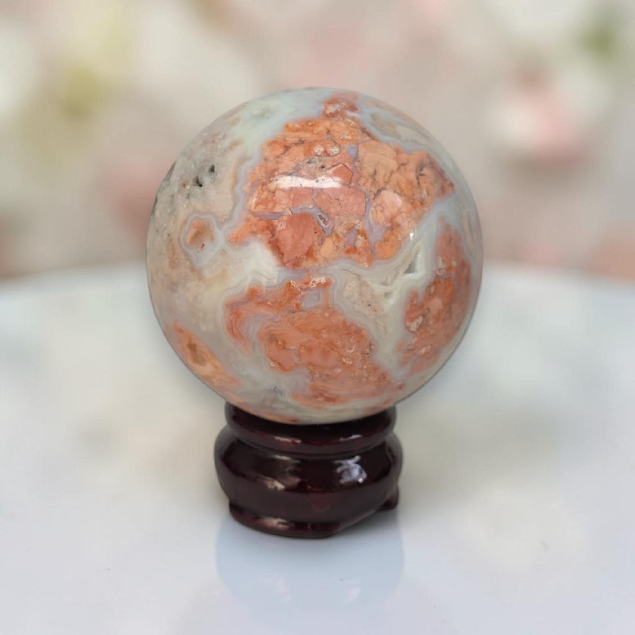 Speckled agate sphere with warm orange bands and creamy white areas on dark stand